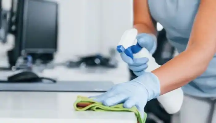 A professional cleaning services showcase representing Home Service Industries by Grow Factor LLC, featuring a close-up of a worker wearing blue protective gloves holding a spray bottle and wiping down a clean white counter surface with a green microfiber cloth.