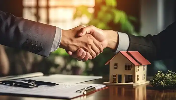 A real estate closing deal graphic representing Real Estate and Property Industries by Grow Factor LLC, showcasing a close-up of a firm handshake between two business individuals in suits over a wooden desk with a miniature house model, a legal document clipboard, and two pens.