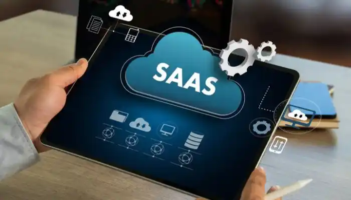A cloud computing concept graphic representing Technology and SaaS Industries by Grow Factor LLC, showcasing an individual holding a tablet device that displays a prominent blue virtual cloud labeled "SAAS" surrounded by digital icons for data storage servers, networks, folders, software integrations, and white gears.